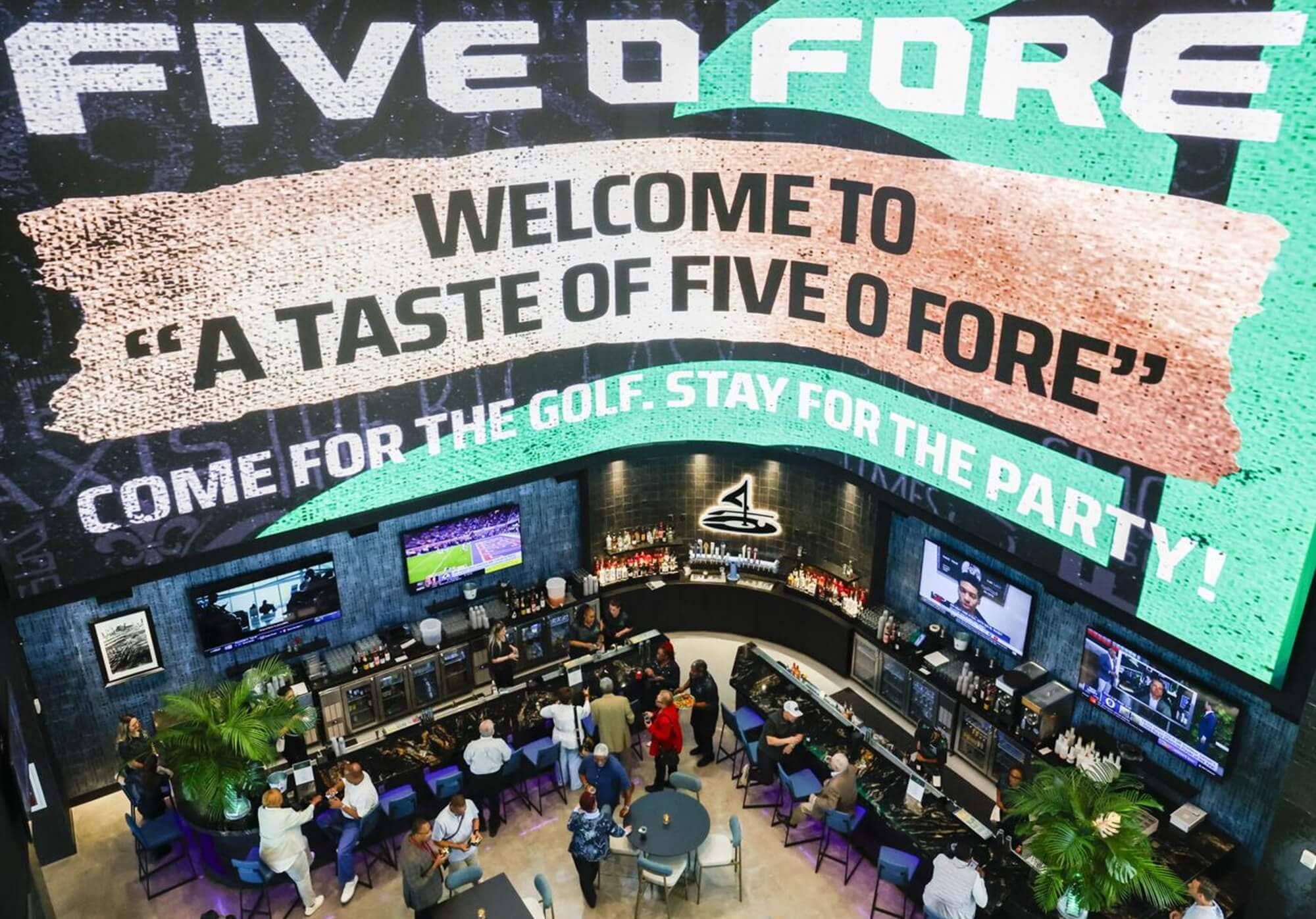 Five O Foreの店内バーエリア。大型スクリーンに「WELCOME TO A TASTE OF FIVE O FORE」と表示され、ゴルフとパーティーを楽しめる空間が広がっている。